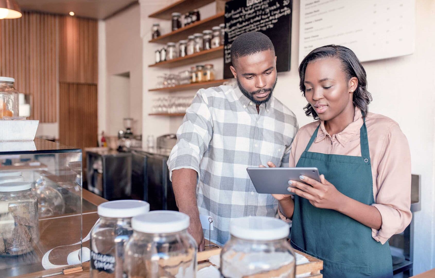 Two young African entrepreneurs working together on a digital tablet at the checkout counter of their trendy cafe