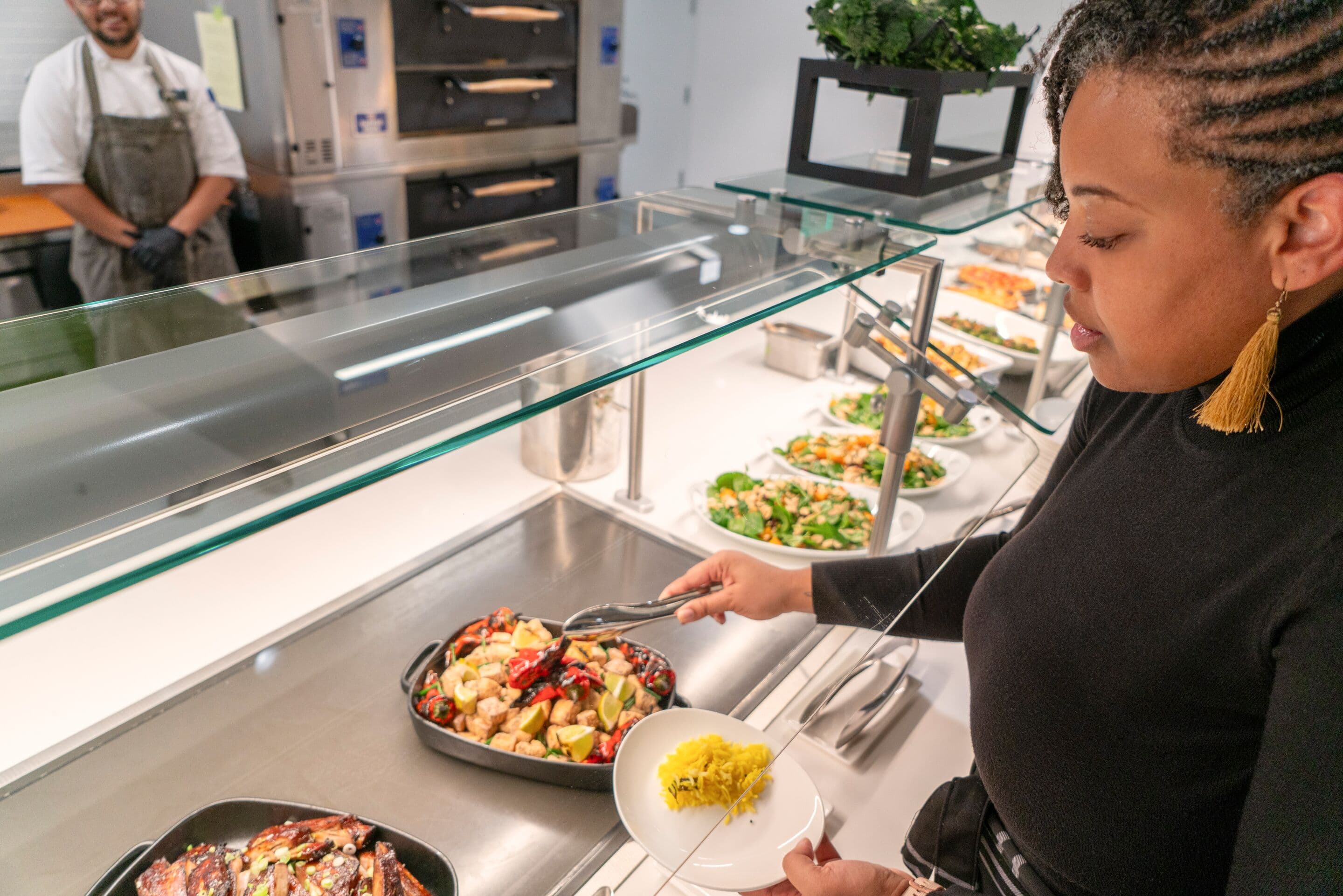 Employee serves themselves a variety of colorful, ethnic dishes, prepared with sustainable locally sourced ingredients.
